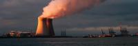 A power plant on a sea shore with smoke emerging from the towers.