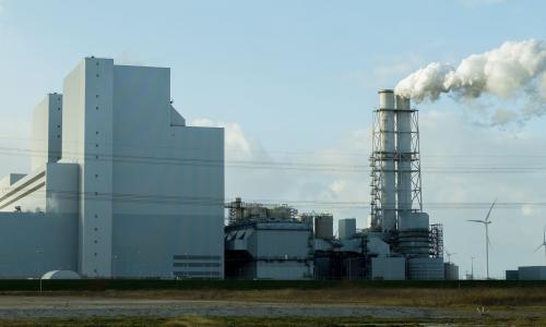 A power plant with wind mills and a smoke column in the center.