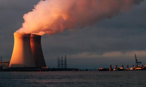 A power plant on a sea shore with smoke emerging from the towers.
